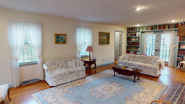 living room featuring light wood-type flooring, a textured ceiling, and french doors