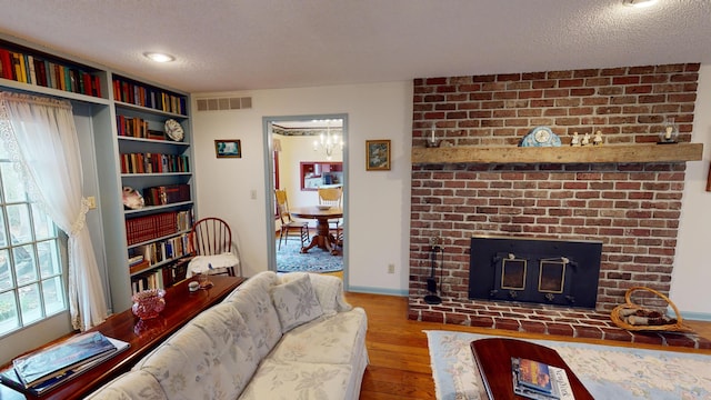 living room featuring hardwood / wood-style floors, an inviting chandelier, a textured ceiling, and a brick fireplace