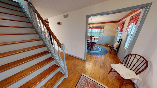 stairway with wood-type flooring and an inviting chandelier