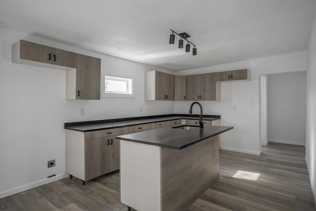 kitchen with dark hardwood / wood-style flooring, rail lighting, a kitchen island with sink, and sink