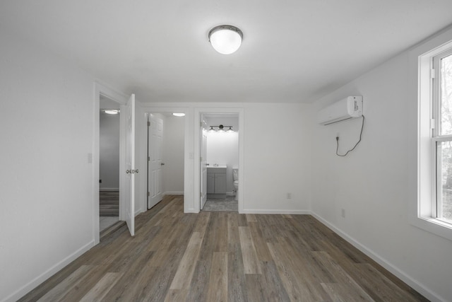 unfurnished bedroom featuring dark hardwood / wood-style flooring, ensuite bath, and an AC wall unit