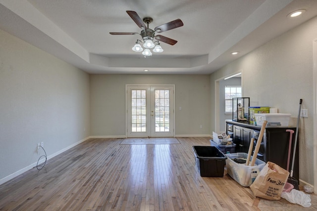 unfurnished living room with french doors, light wood-type flooring, a tray ceiling, and ceiling fan