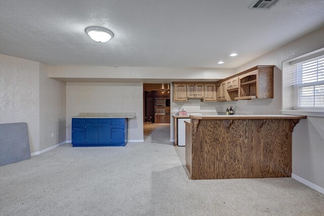 kitchen with a breakfast bar area, kitchen peninsula, light colored carpet, and a textured ceiling