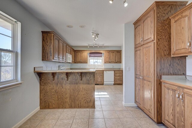 kitchen featuring a breakfast bar, white appliances, kitchen peninsula, and a wealth of natural light