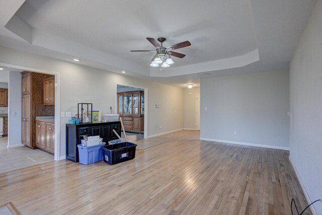 living room featuring a raised ceiling, ceiling fan, and light hardwood / wood-style floors