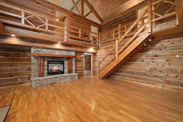 unfurnished living room with wood walls, wooden ceiling, high vaulted ceiling, a stone fireplace, and wood-type flooring