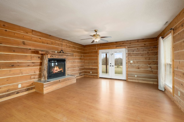 unfurnished living room with french doors, a textured ceiling, ceiling fan, wooden walls, and light hardwood / wood-style floors