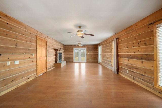 unfurnished living room with wood walls, french doors, ceiling fan, and hardwood / wood-style flooring