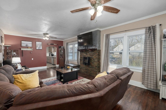 living room featuring a stone fireplace, dark hardwood / wood-style floors, ceiling fan, ornamental molding, and a textured ceiling