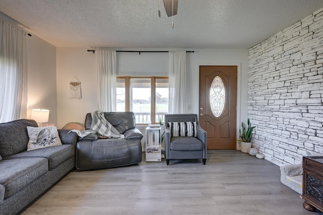 living room with a textured ceiling, light wood-type flooring, and ceiling fan