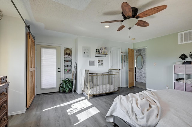 bedroom with a textured ceiling, ceiling fan, a barn door, a nursery area, and dark hardwood / wood-style floors