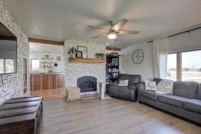 living room featuring a stone fireplace, a wealth of natural light, light hardwood / wood-style flooring, and a textured ceiling