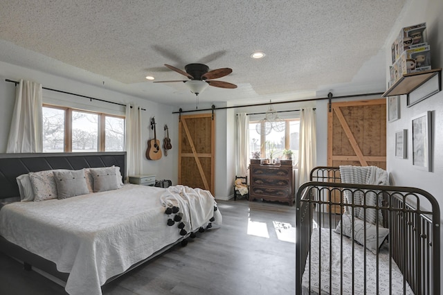 bedroom featuring a barn door, ceiling fan, wood-type flooring, and multiple windows