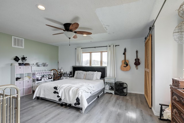 bedroom featuring wood-type flooring, a barn door, a textured ceiling, and ceiling fan