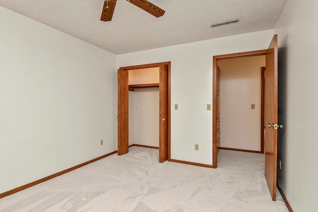 unfurnished bedroom with ceiling fan, a closet, light colored carpet, and a textured ceiling