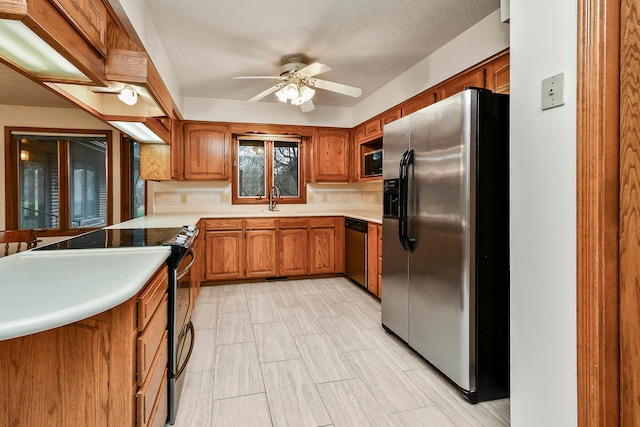 kitchen featuring ceiling fan, sink, kitchen peninsula, a textured ceiling, and appliances with stainless steel finishes