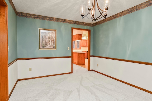 carpeted spare room featuring a textured ceiling and an inviting chandelier