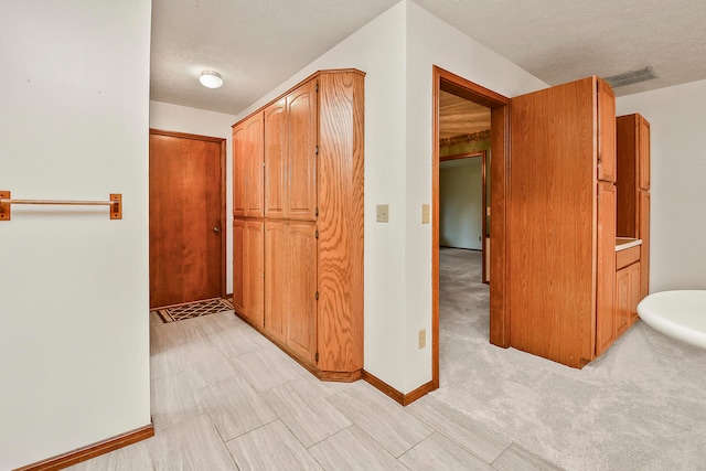 hallway with a textured ceiling and light carpet