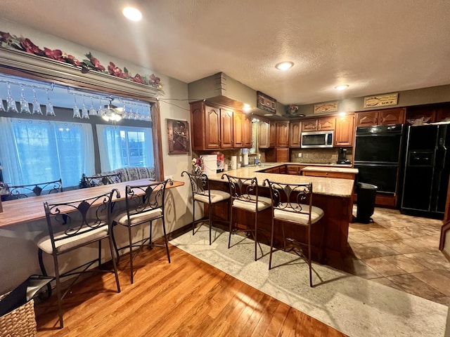 kitchen featuring double oven, kitchen peninsula, light hardwood / wood-style floors, a textured ceiling, and a breakfast bar