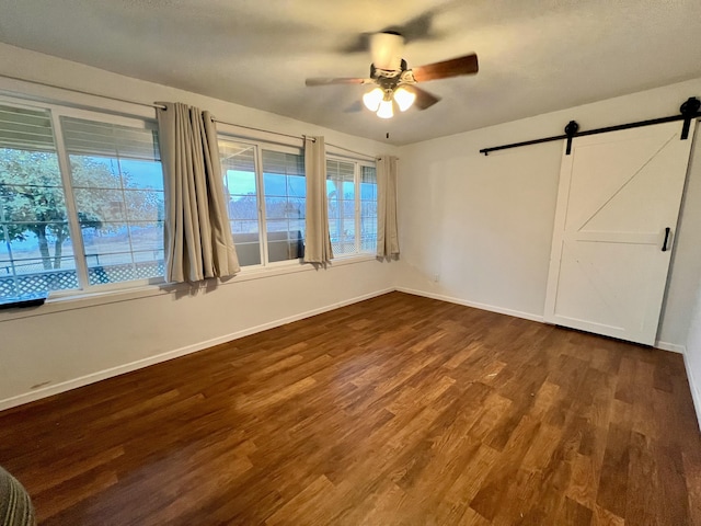 unfurnished bedroom with a barn door, ceiling fan, and dark wood-type flooring