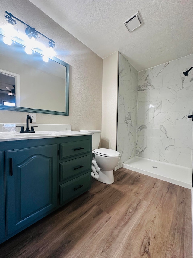 bathroom with hardwood / wood-style floors, vanity, toilet, a textured ceiling, and a tile shower