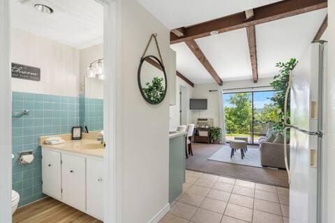 bathroom with tile walls, vanity, toilet, tile patterned floors, and beam ceiling