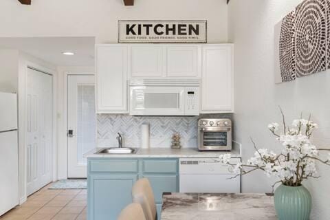 kitchen featuring tasteful backsplash, white cabinetry, sink, light tile patterned floors, and white appliances