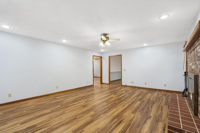 unfurnished living room with ceiling fan, dark wood-type flooring, and a brick fireplace