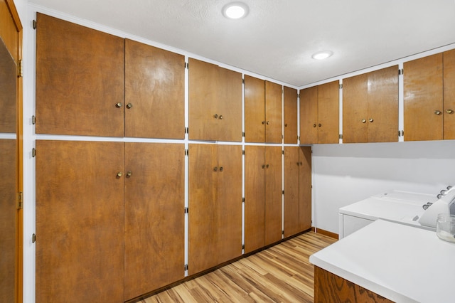 laundry area with cabinets, a textured ceiling, washing machine and dryer, and light hardwood / wood-style flooring