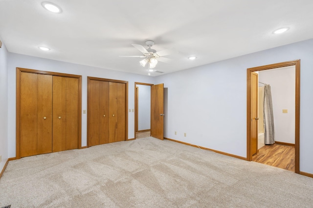 unfurnished bedroom featuring light carpet, two closets, ensuite bath, and ceiling fan