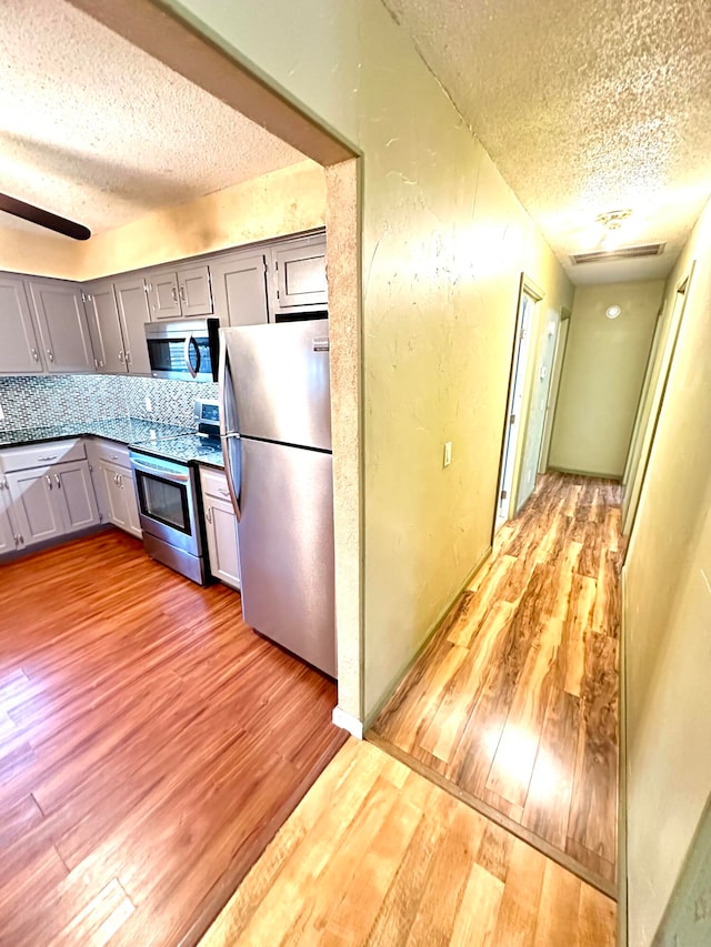 kitchen featuring a textured ceiling, light hardwood / wood-style floors, stainless steel appliances, and tasteful backsplash