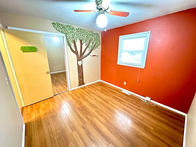 unfurnished bedroom with a closet, ceiling fan, hardwood / wood-style floors, and a textured ceiling