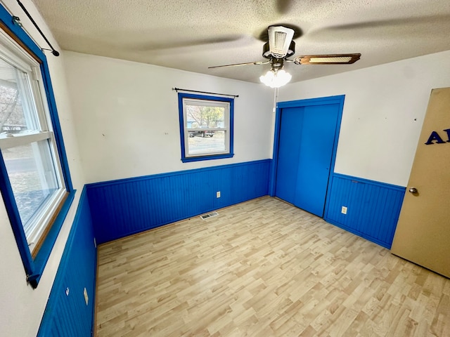 empty room featuring ceiling fan, wood walls, a textured ceiling, and light hardwood / wood-style flooring