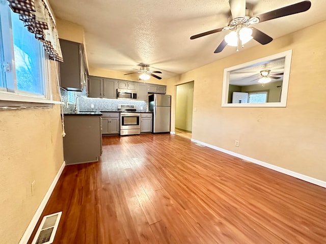 kitchen featuring gray cabinetry, sink, hardwood / wood-style flooring, tasteful backsplash, and stainless steel appliances