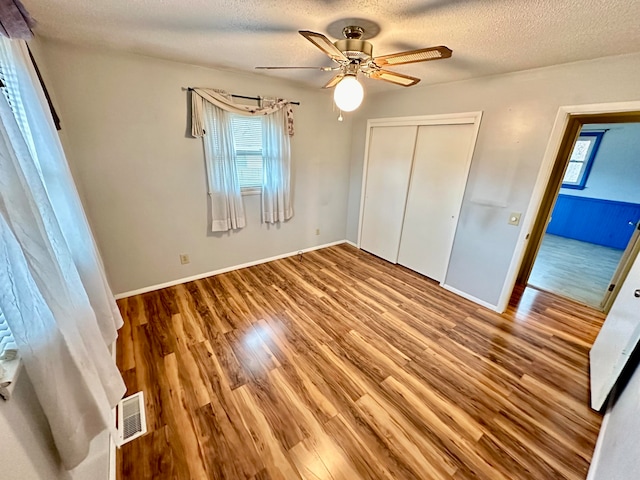 unfurnished bedroom featuring hardwood / wood-style floors, ceiling fan, a textured ceiling, and a closet