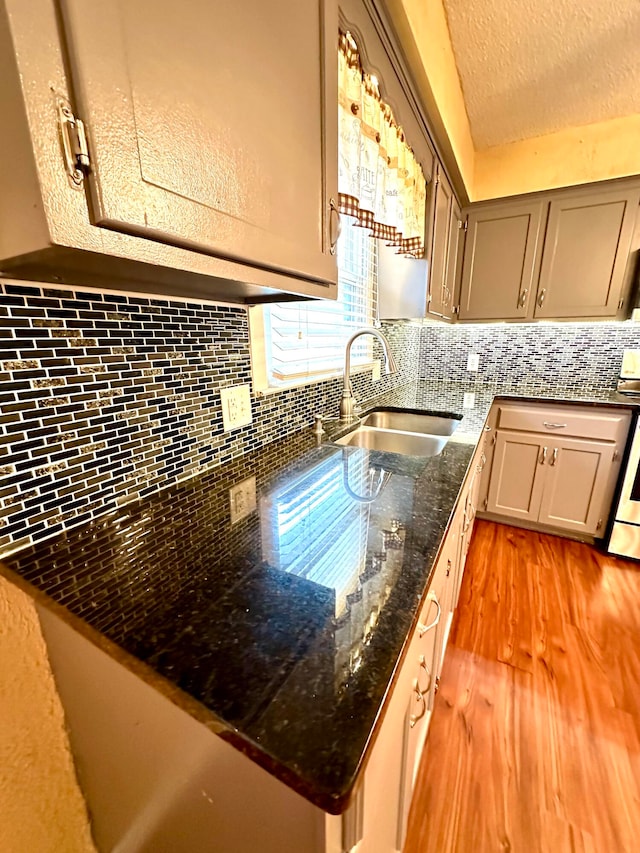 kitchen with decorative backsplash, dark stone counters, a textured ceiling, sink, and light hardwood / wood-style floors