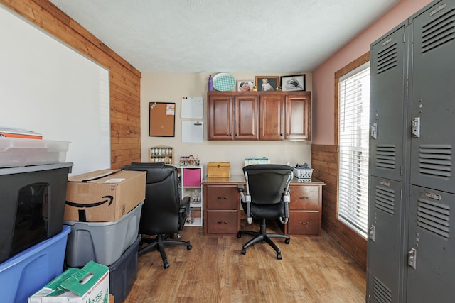 office featuring a textured ceiling, wooden walls, and light hardwood / wood-style flooring