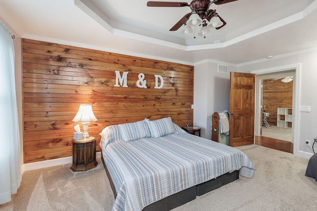 carpeted bedroom featuring ceiling fan, wood walls, ornamental molding, and a tray ceiling