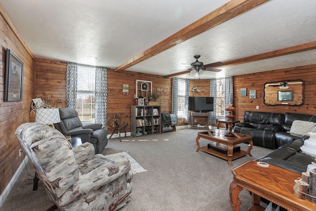 living room featuring wood walls, ceiling fan, a textured ceiling, beam ceiling, and carpet floors