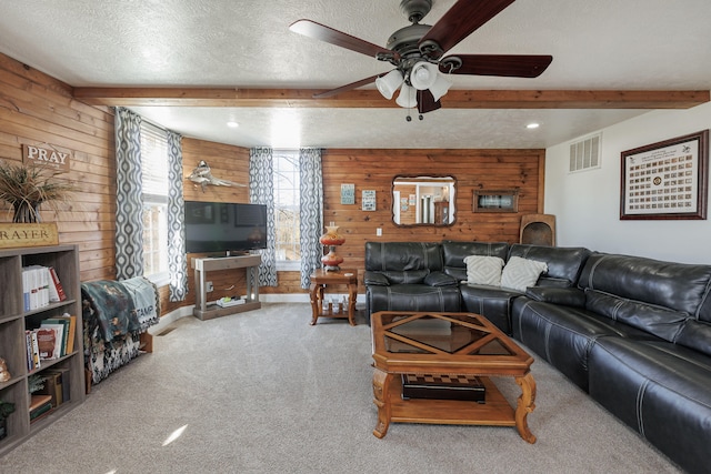 living room featuring wood walls, beamed ceiling, light colored carpet, and a textured ceiling