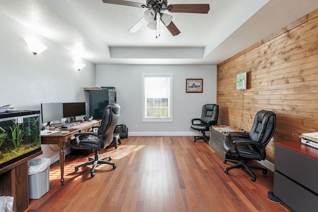 office with ceiling fan, wood walls, wood-type flooring, and a tray ceiling