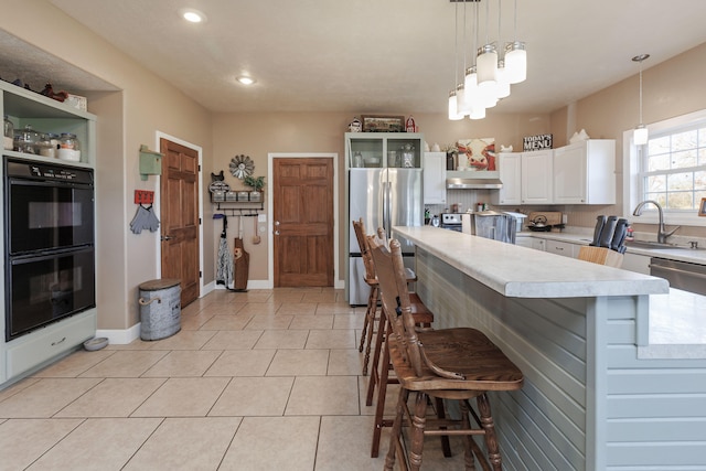 kitchen with pendant lighting, white cabinets, light tile patterned floors, a kitchen bar, and stainless steel appliances