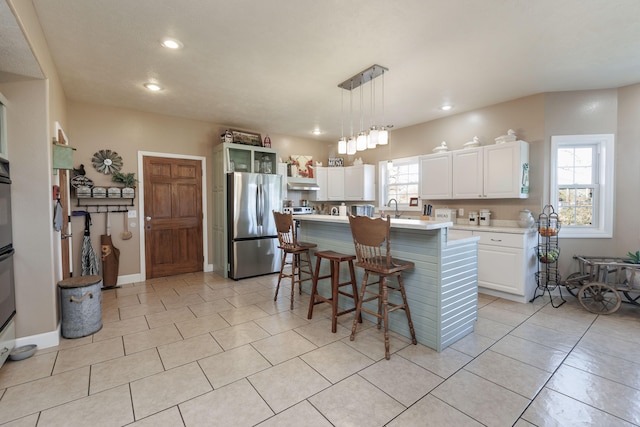 kitchen featuring a breakfast bar, a kitchen island with sink, decorative light fixtures, white cabinets, and stainless steel refrigerator