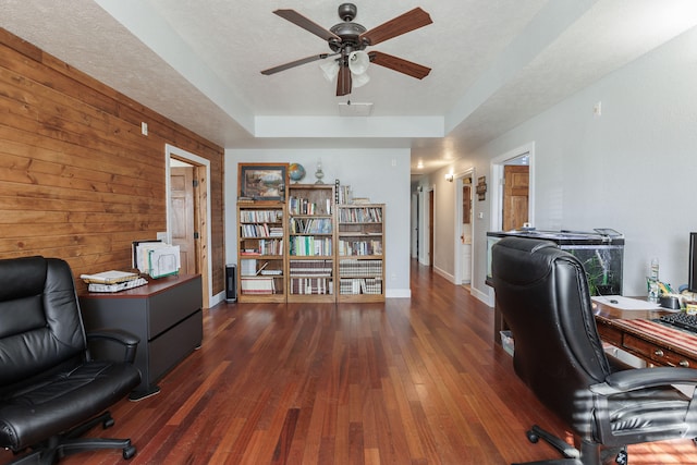 office area with a textured ceiling, ceiling fan, dark wood-type flooring, and wooden walls