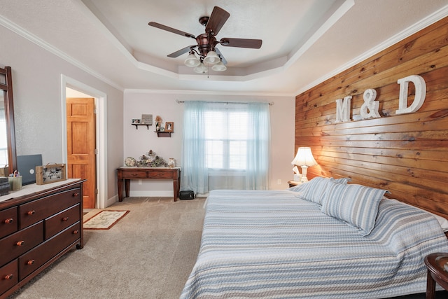 carpeted bedroom with a tray ceiling, ceiling fan, wood walls, and ornamental molding