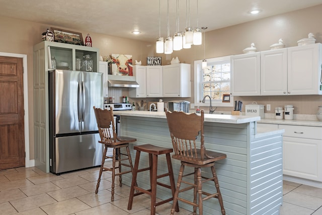 kitchen with a kitchen island with sink, range hood, decorative light fixtures, white cabinetry, and stainless steel refrigerator