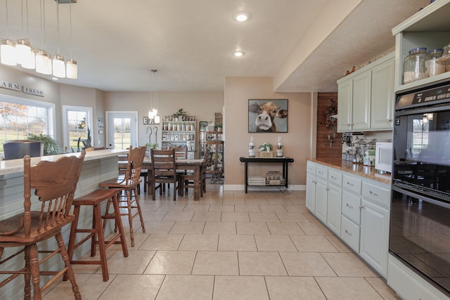 kitchen featuring white cabinets, decorative light fixtures, light tile patterned flooring, and black double oven