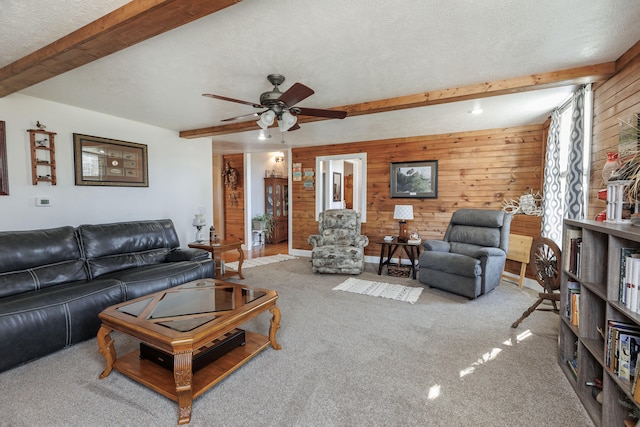 carpeted living room featuring beamed ceiling, a textured ceiling, ceiling fan, and wood walls