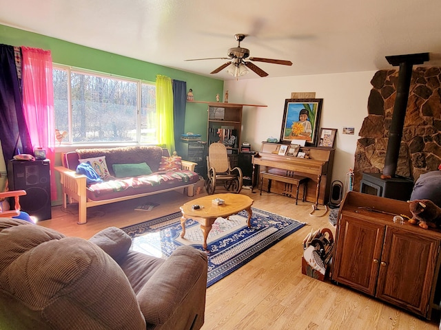 living room with wood finished floors, a wood stove, and a ceiling fan