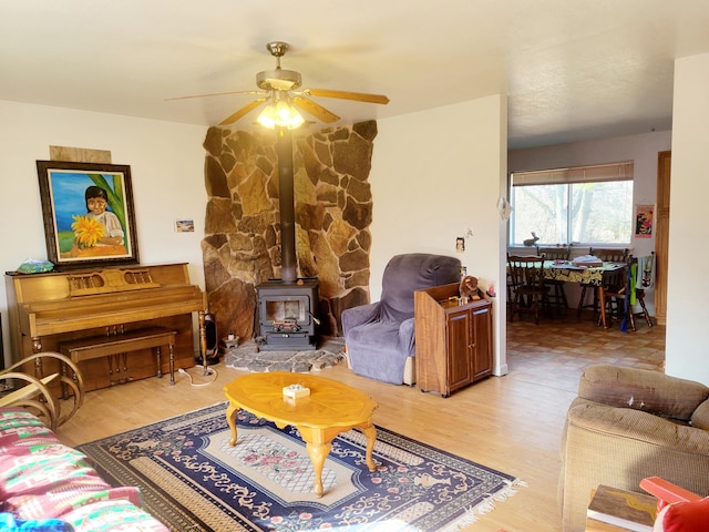 living area with ceiling fan, light wood finished floors, and a wood stove